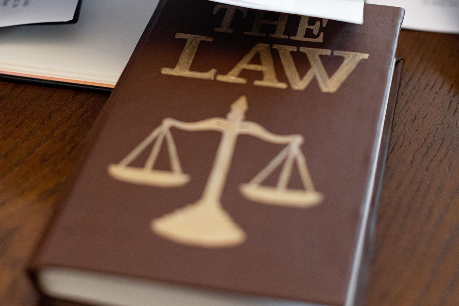 A brown book titled The Law, with a scales mark, on a wooden desk